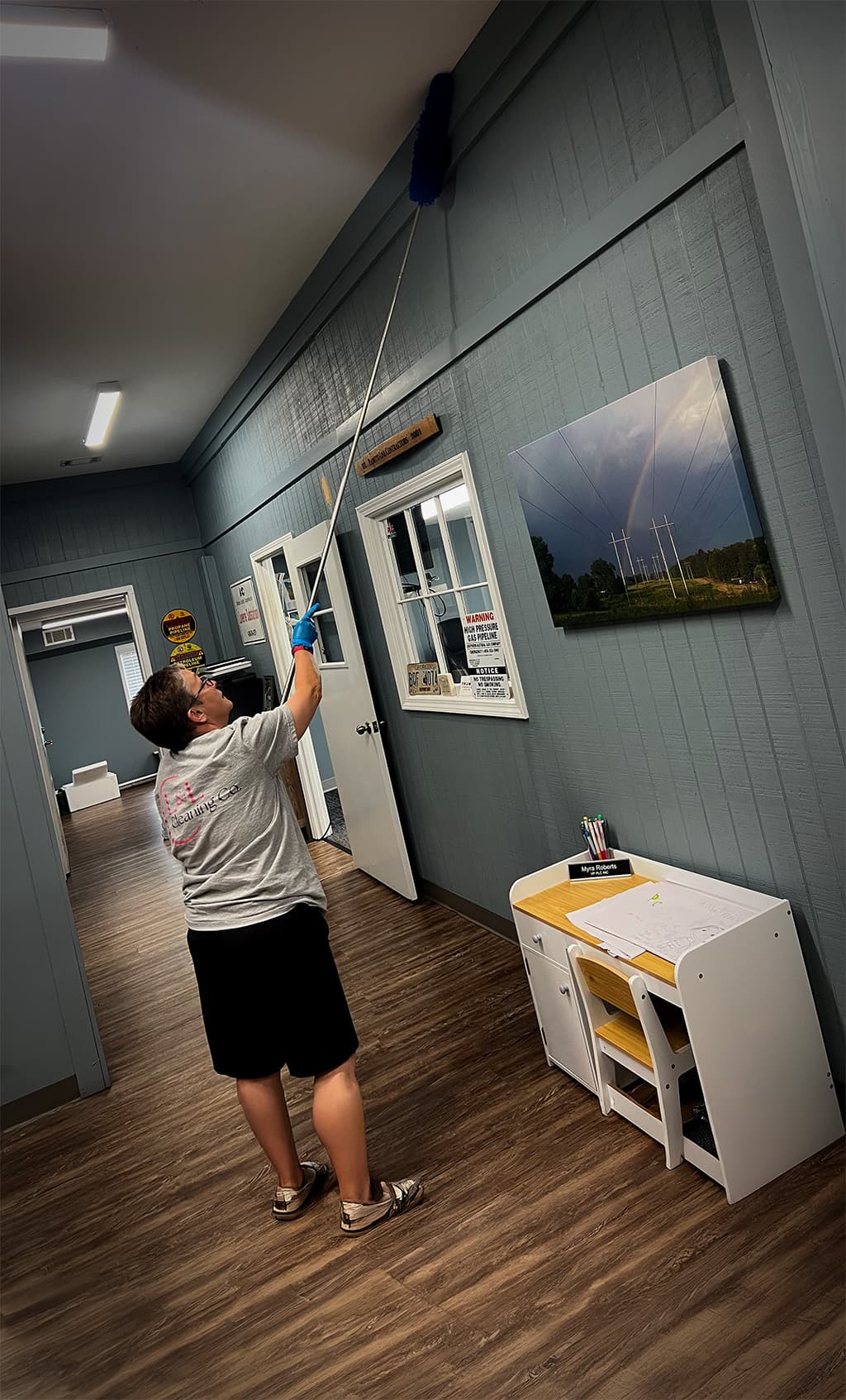 A woman going the extra mile to dust crown molding in an office.